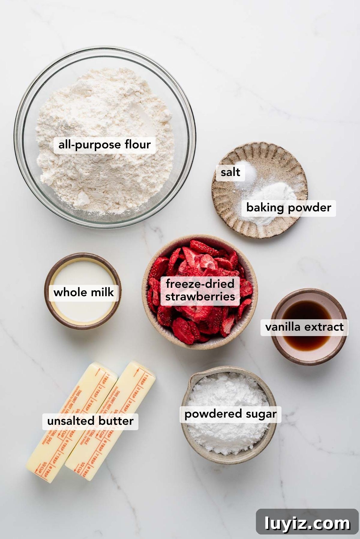 Strawberry Shortbread Cookie Recipe for Tender, Buttery Cookies 4 Ingredients in various size bowls and plates labeled as all purpose flour, salt, baking powder, whole milk, freeze dried strawberries, vanilla extract, unsalted butter, and powdered sugar on a white marbled background.