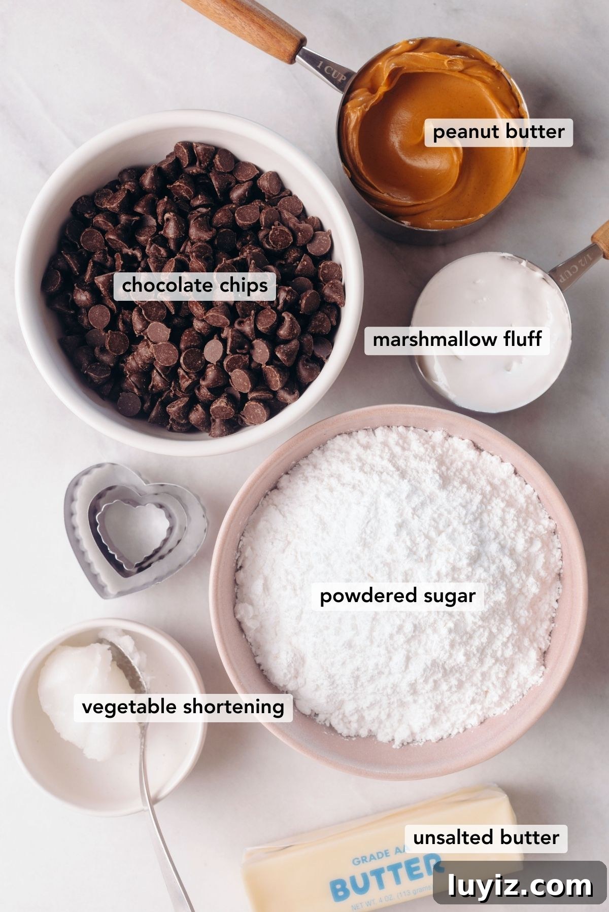 Chocolate-Covered Peanut Butter Heart Truffles 3 Ingredients needed for chocolate covered peanut butter eggs with three heart-shaped cookie cutters on a white marbled background.