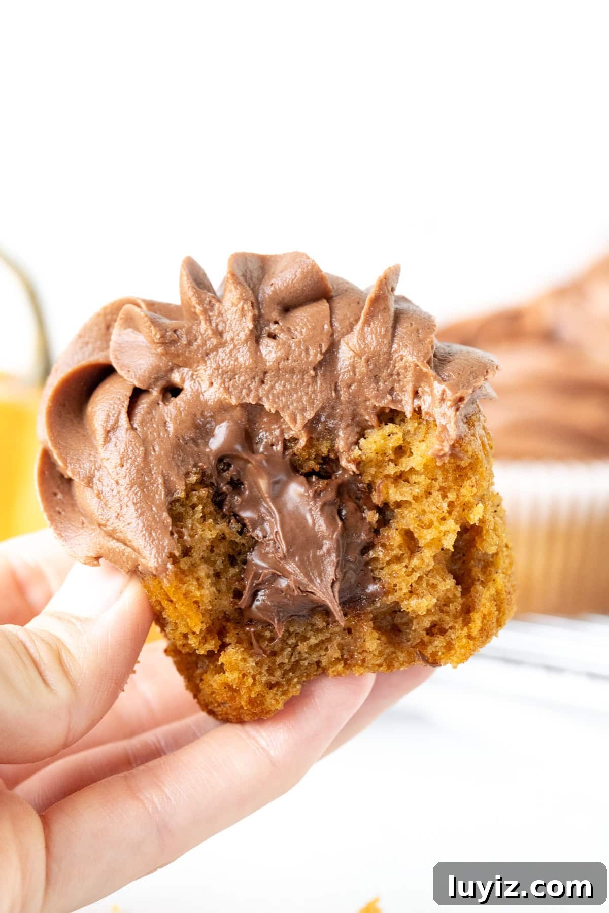 Nutella-Stuffed Pumpkin Cupcakes with Cream Cheese Frosting 5 Nutella pumpkin cupcake with a bite taken out and oozing with Nutella, held in a hand