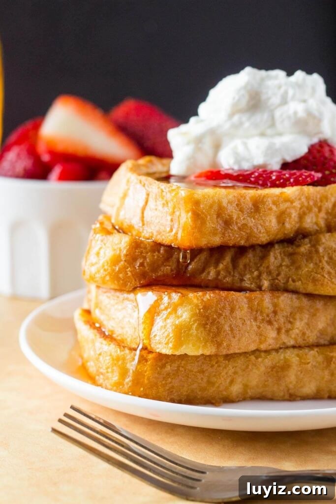Classic French Toast Recipe: Crispy Golden Brunch Favorite 3 A tall stack for french toast topped with whipped cream and strawberries, then drizzled in maple syrup.
