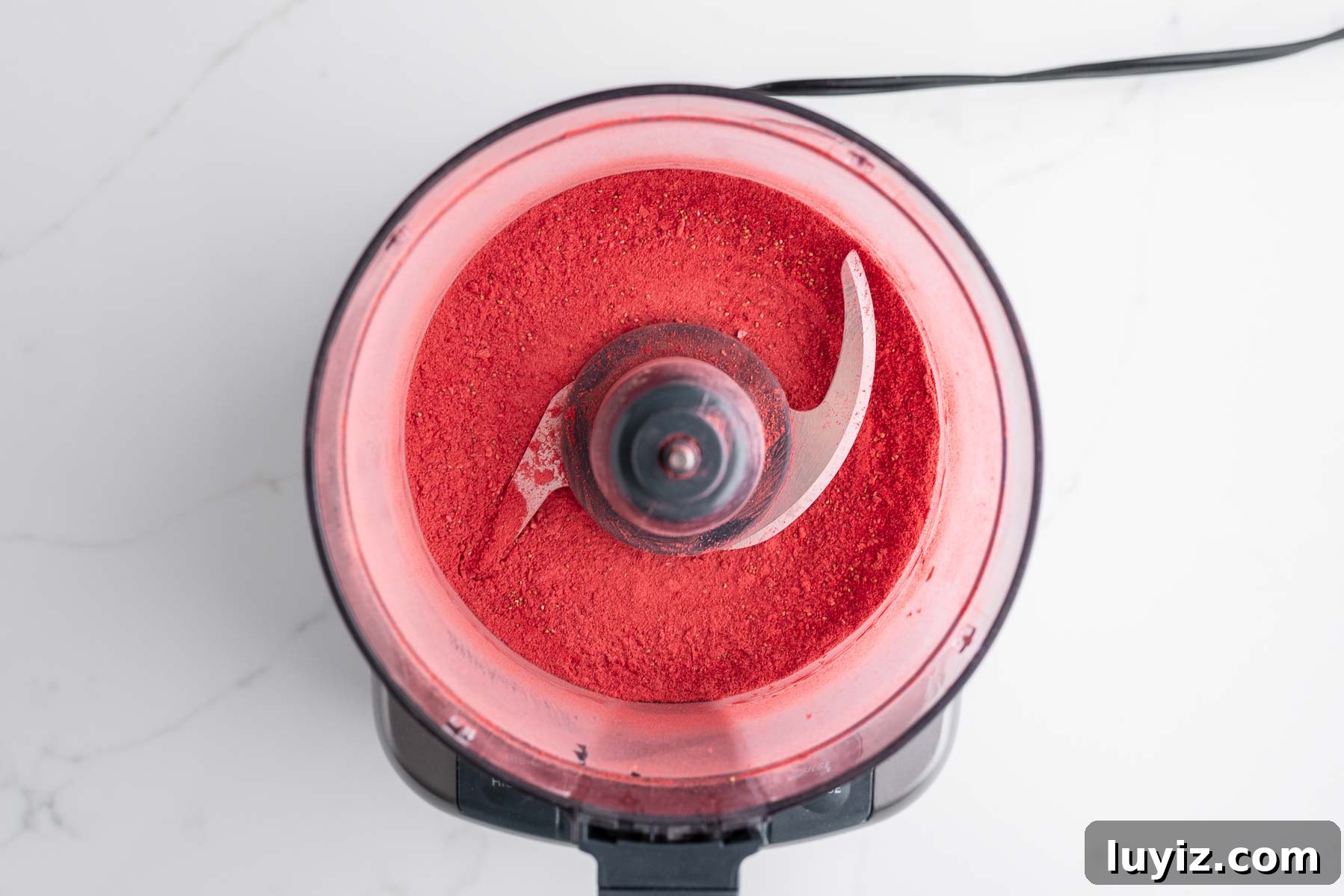 Creamy Homemade Strawberry Ice Cream Recipe You’ll Love 5 Processed freeze-dried strawberries in a medium-sized food processor on a white marbled background.