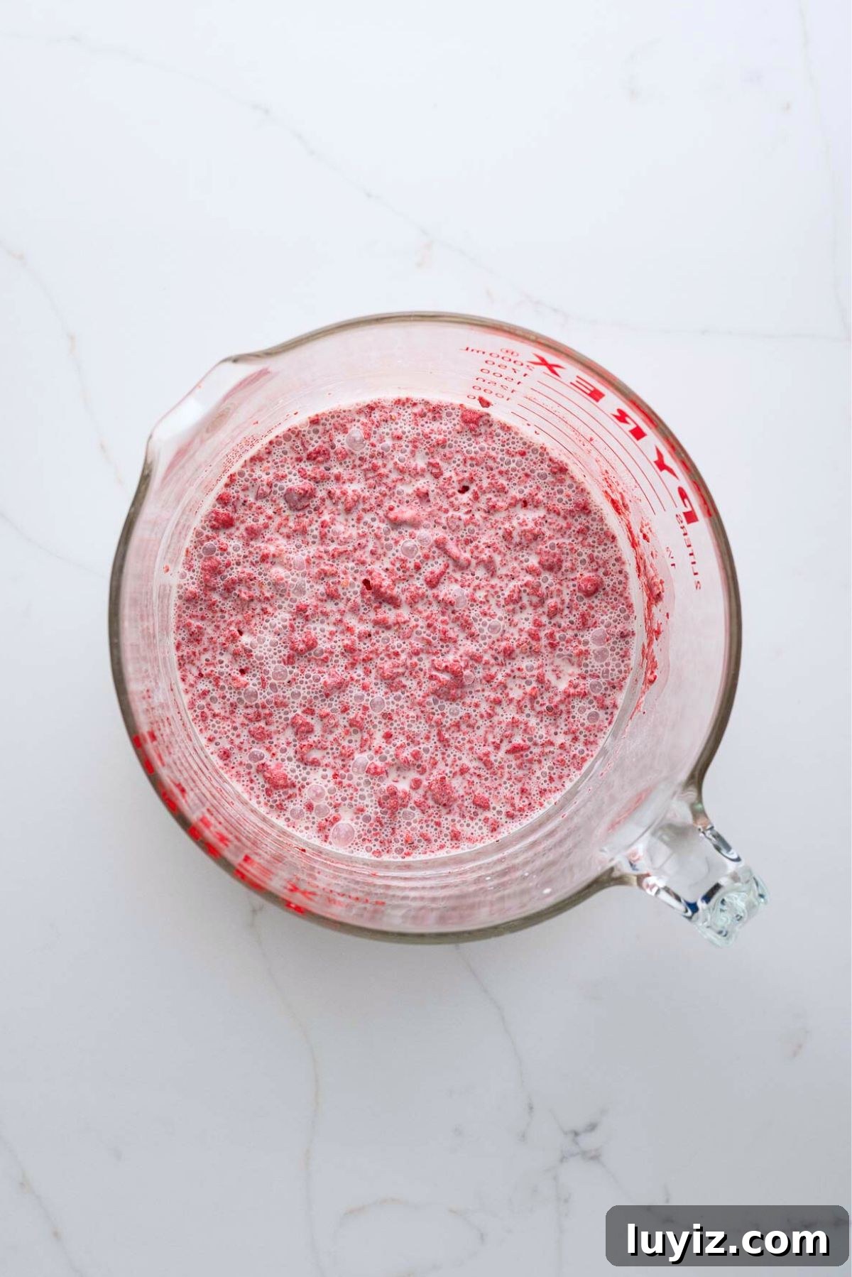 Creamy Homemade Strawberry Ice Cream Recipe You’ll Love 7 Strawberry ice cream base mixed all together in a large glass mixing bowl on a white marbled background.