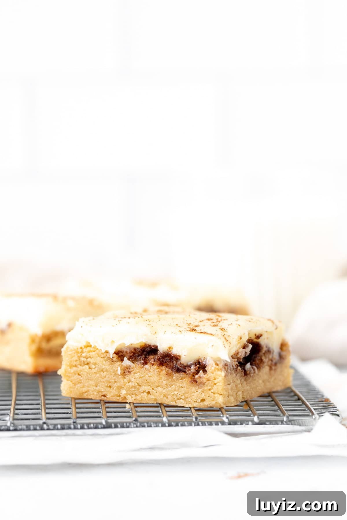 Cinnamon Roll Blondies Recipe — Gooey Swirl Dessert Bars 7 Cinnamon roll blondies with cream cheese frosting on a cooling rack