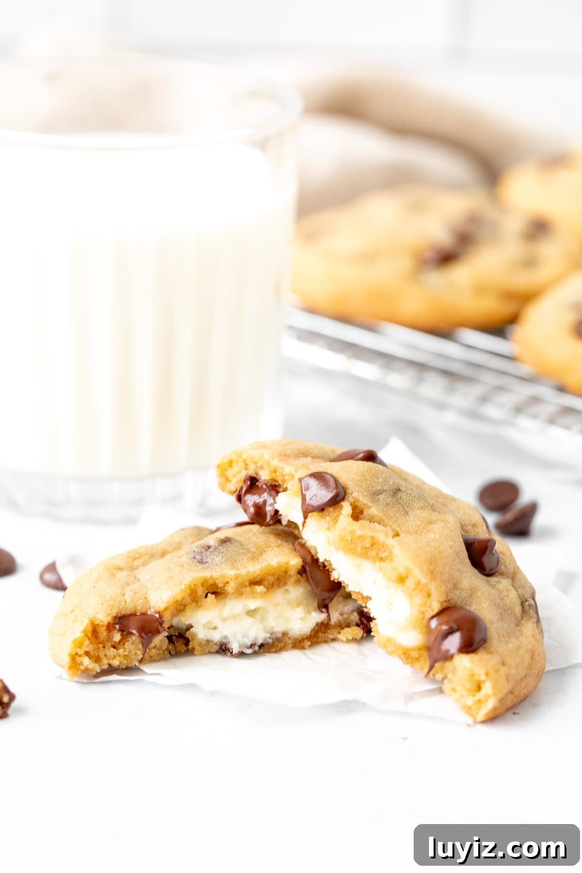 Cheesecake-Stuffed Chocolate Chip Cookies — Decadent Dessert Recipe 3 cheesecake stuffed chocolate chip cookie, broken in half with glass of milk