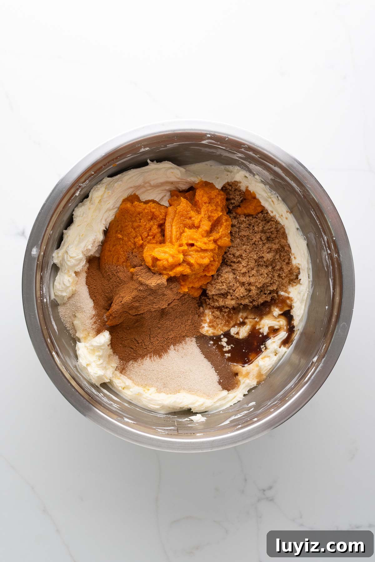 Creamy Pumpkin Cheesecake Recipe for Fall Desserts 12 Pumpkin puree, granulated sugar, light brown sugar, vanilla extract, cinnamon, sour cream, and pumpkin pie spice added to the whipped cream in a stainless steel mixing bowl.