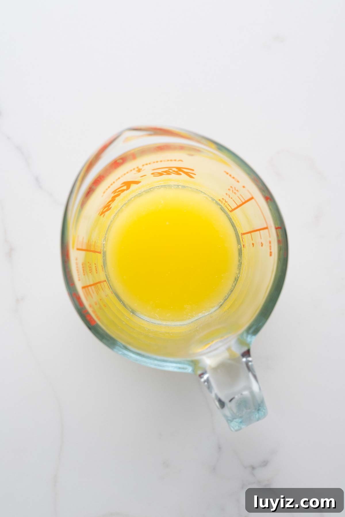 Creamy Pumpkin Cheesecake Recipe for Fall Desserts 5 Melted unsalted butter in a glass measuring cup on a white marbled background.