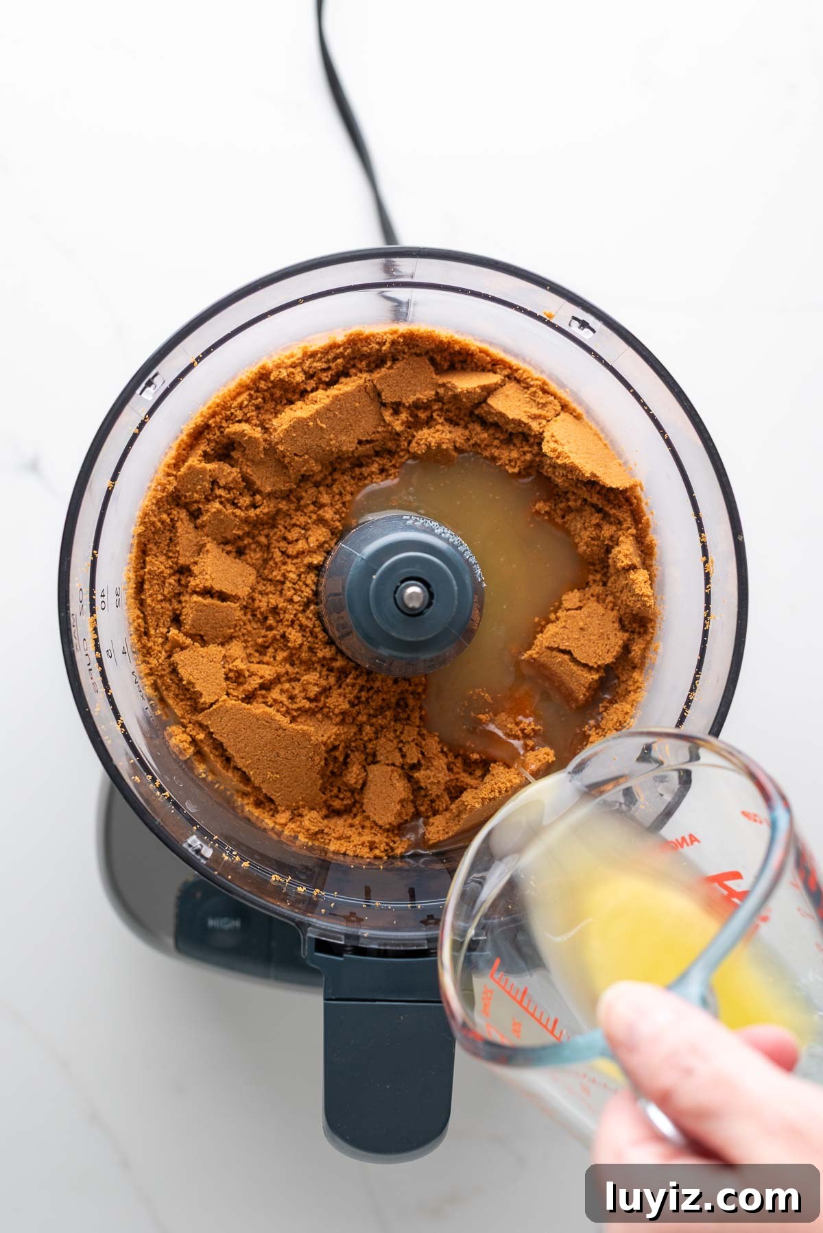 Creamy Pumpkin Cheesecake Recipe for Fall Desserts 7 Adding melted unsalted butter in a glass measuring cup to a food processor with speculoos cookie crumbs.