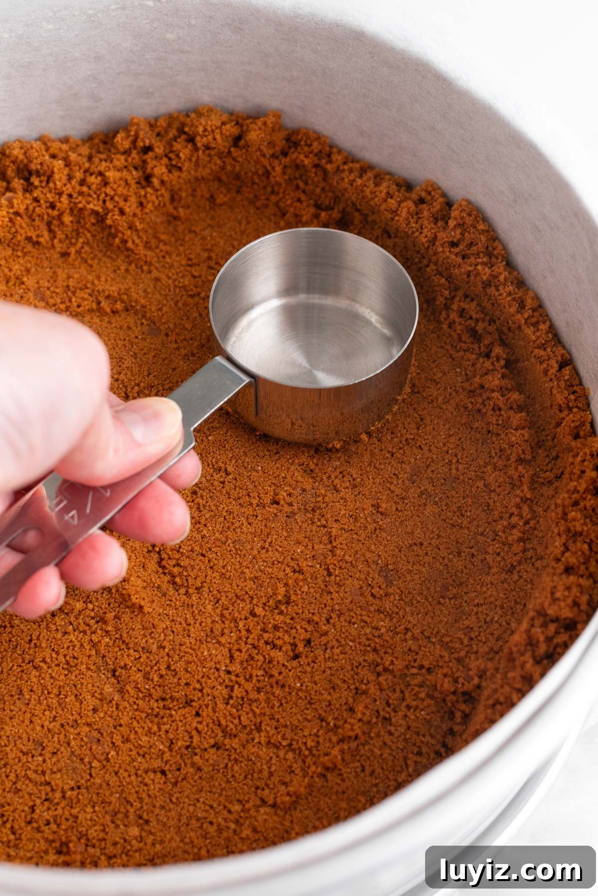 Creamy Pumpkin Cheesecake Recipe for Fall Desserts 8 Forming the speculoos cookie crust in a parchment paper lined springform pan using a small metal measuring cup.