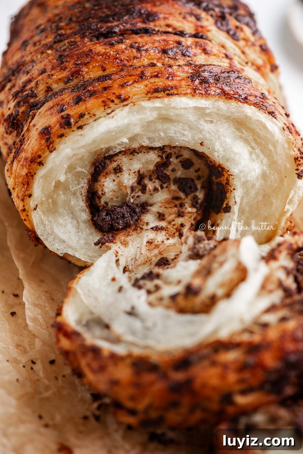 Chocolate Croissant Loaf Recipe: Flaky Chocolate Swirl Bread 2 Chocolate croissant loaf pulled apart to see the inside chocolatey, flaky layers on brown parchment paper.