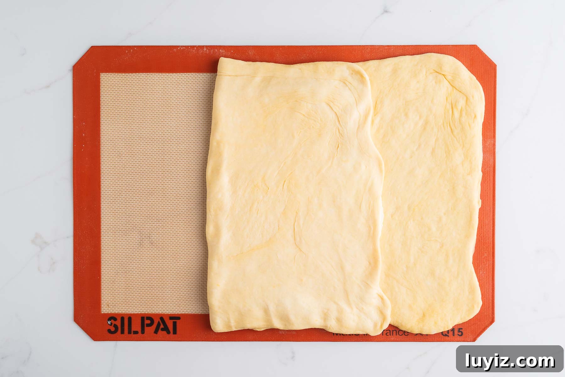 Chocolate Croissant Loaf Recipe: Flaky Chocolate Swirl Bread 11 Left panel of dough folded over the rectangular slab of butter on a silicone baking sheet.