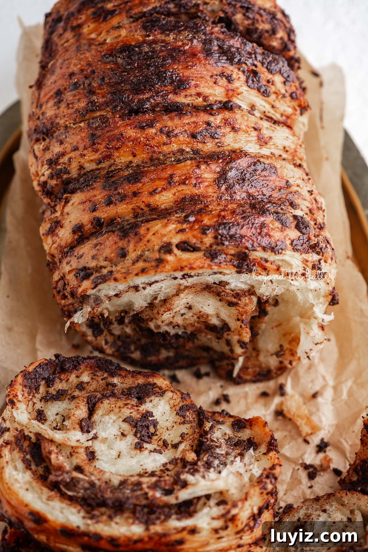 Chocolate Croissant Loaf Recipe: Flaky Chocolate Swirl Bread 19 Sliced chocolate croissant bread loaf on brown parchment paper lined gold tray and white marbled background.