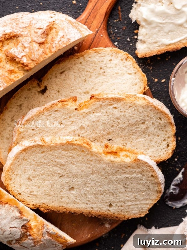 Chocolate Croissant Loaf Recipe: Flaky Chocolate Swirl Bread 20 Slices of crusty fresh french bread on a round wooden cutting board next to a small bowl of butter and light beige cloth napkin on a black background.