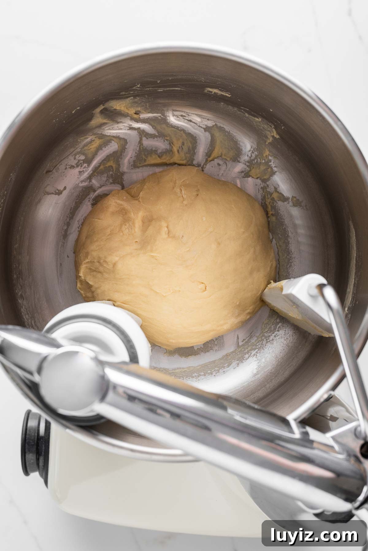 Chocolate Croissant Loaf Recipe: Flaky Chocolate Swirl Bread 7 Mixing bread flour, warm milk, salt, an egg, melted unsalted butter, sugar, and yeast in an Ankasrum Assistent Original Mixer on a white marbled background.