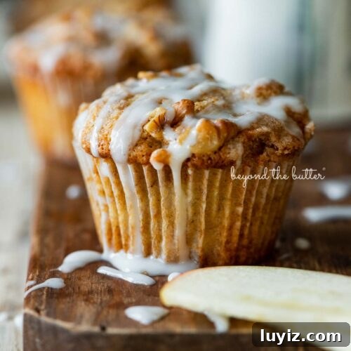 Warm apple cinnamon streusel muffins on a wood cutting board with slices of apples and vanilla glaze.