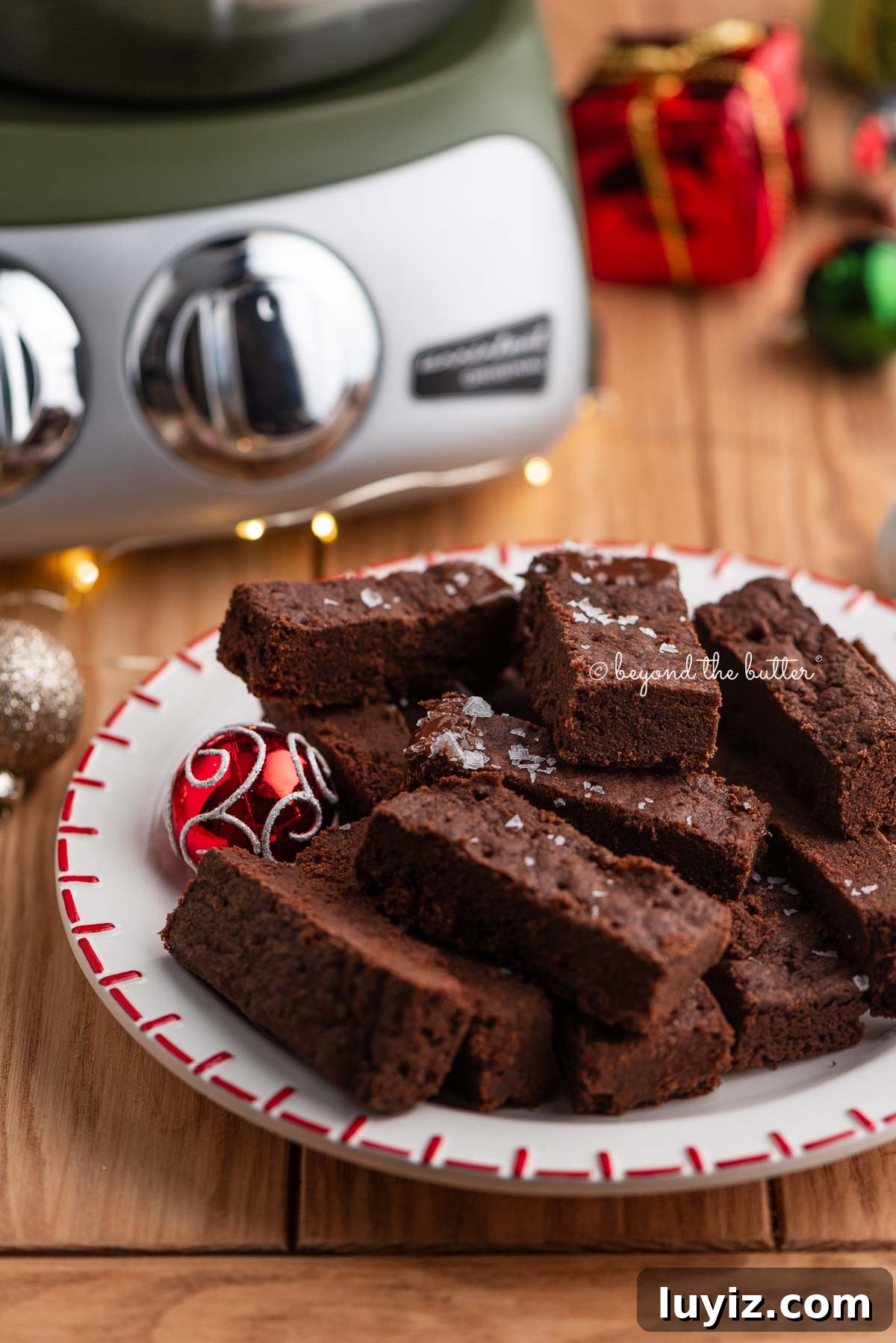 Classic Chocolate Shortbread Cookies Recipe for Homemade Treats 5 Red and white dessert plate topped with chocolate shortbread surrounded by miniature ball ornaments, fairy lights, and a forest green Ankarsrum Assistent Original mixer on a natural wood background.
