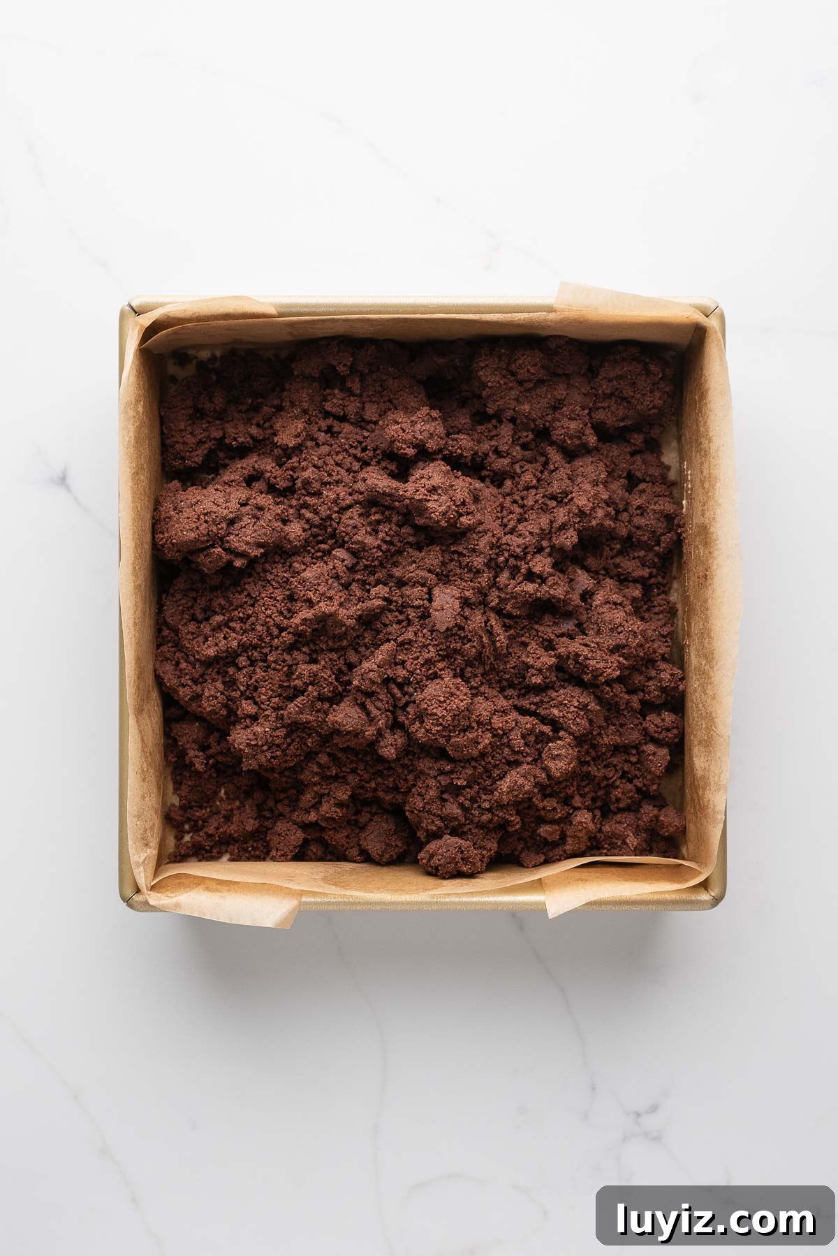 Classic Chocolate Shortbread Cookies Recipe for Homemade Treats 10 Chocolate shortbread dough transferred to a parchment paper lined eight inch square baking tin on a white marbled surface.