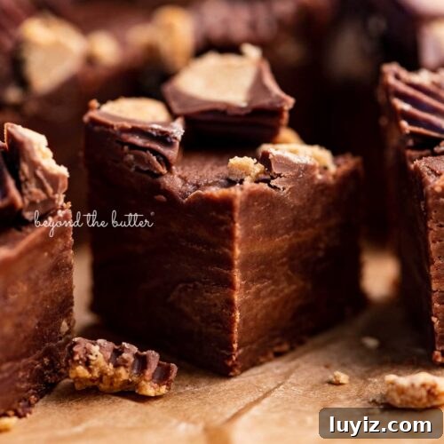 Close up of 1 inch cubes of homemade chocolate peanut butter fudge on brown parchment paper.