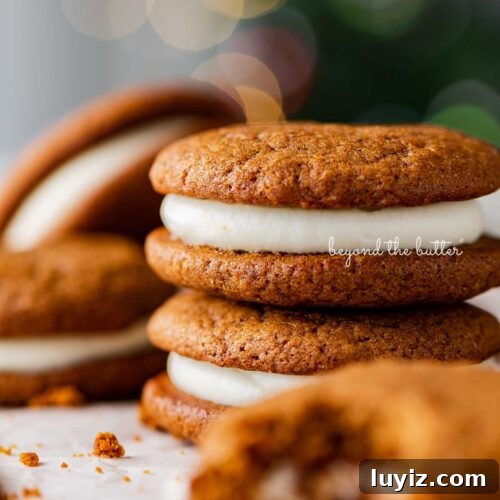 Stacked gingerbread whoopie pies on white parchment paper with holiday tree background.