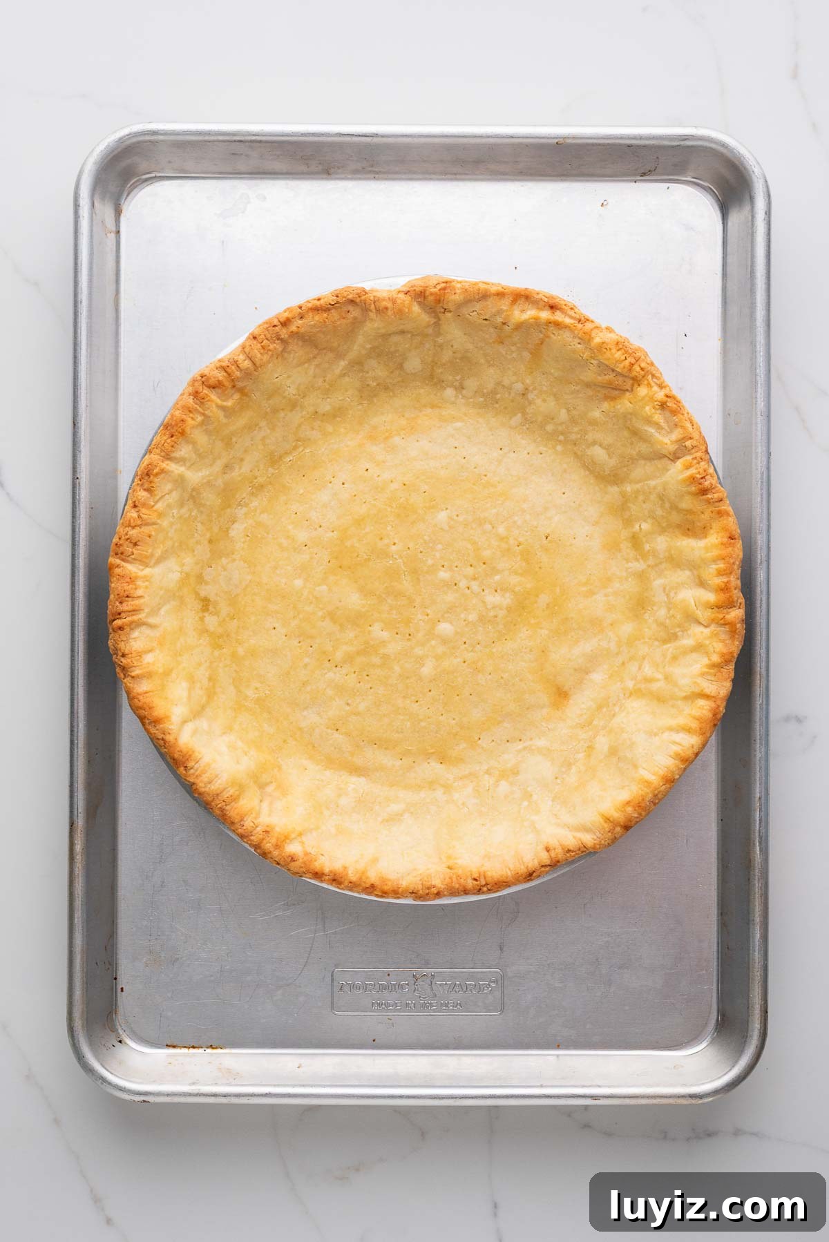 Lemon Cream Pie Recipe: Silky No-Bake Dessert Tutorial 15 Blind baked pie crust in a metal pie in placed on a metal baking sheet and white marbled background.