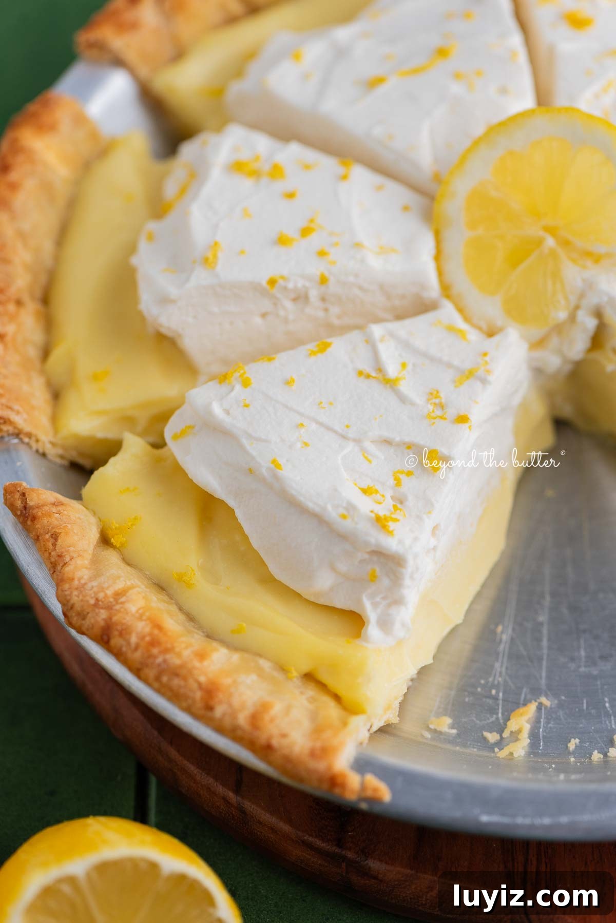 Lemon Cream Pie Recipe: Silky No-Bake Dessert Tutorial 20 Slices of lemon sour cream pie topped with whipped cream and lemon zest in a metal pie tin on a green tiled background.
