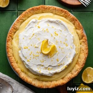 Lemon Cream Pie Recipe: Silky No-Bake Dessert Tutorial 25 Lemon cream pie topped with fresh whipped cream and lemon zest centered on a green tiled background surrounded by lemons, wood dessert plates, forks, napkin, and pie server.