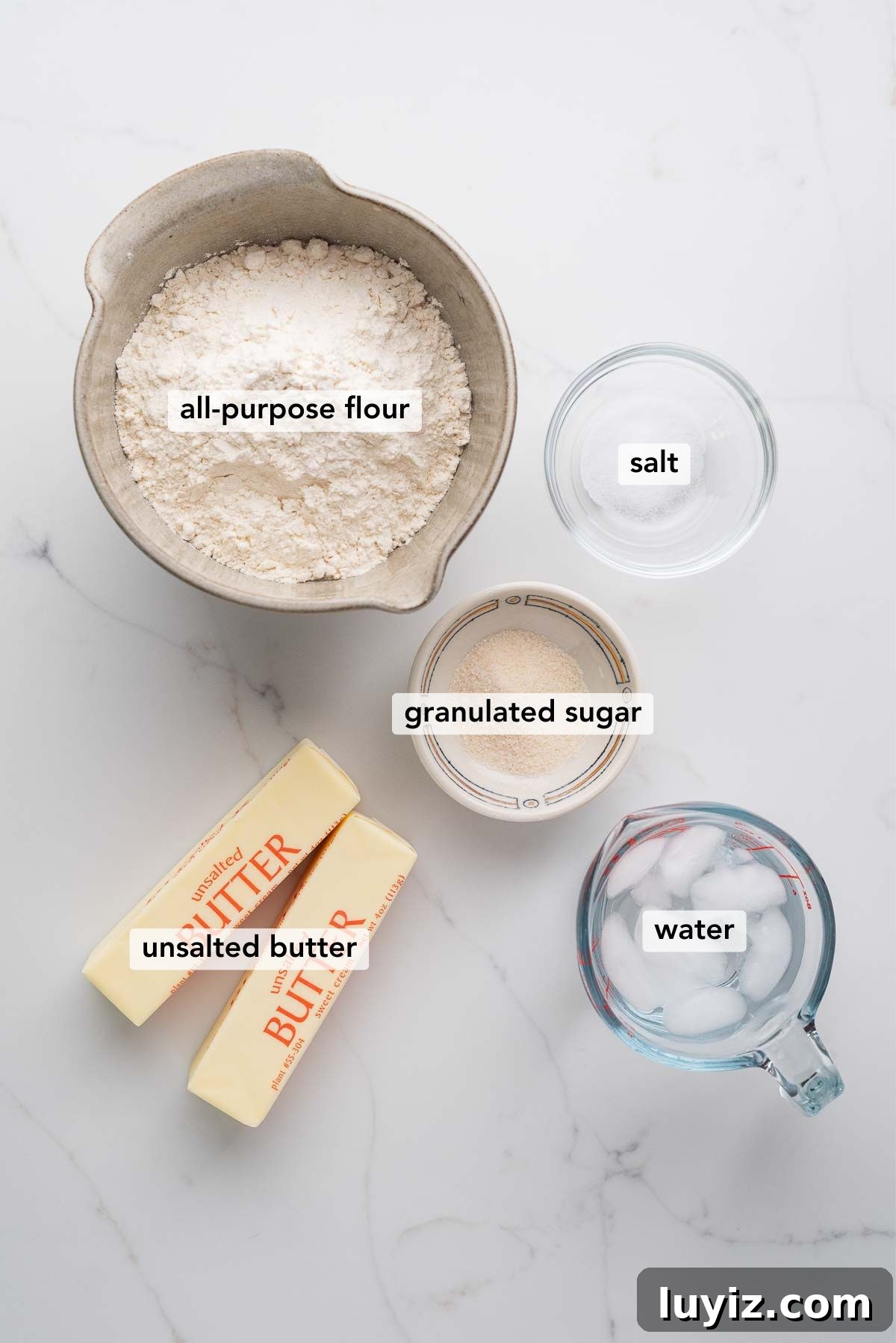 Lemon Cream Pie Recipe: Silky No-Bake Dessert Tutorial 6 Ingredients in various size bowls labeled as all purpose flour, salt, granulated sugar, unsalted butter, and water on a white marbled background.