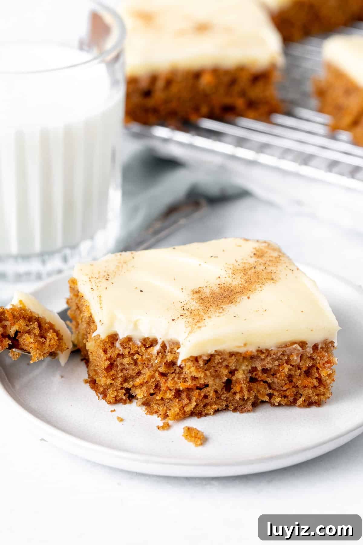 Chewy Carrot Cake Bars with Cream Cheese Frosting 8 Slice of carrot cake bar with a bite taken out with glass of milk