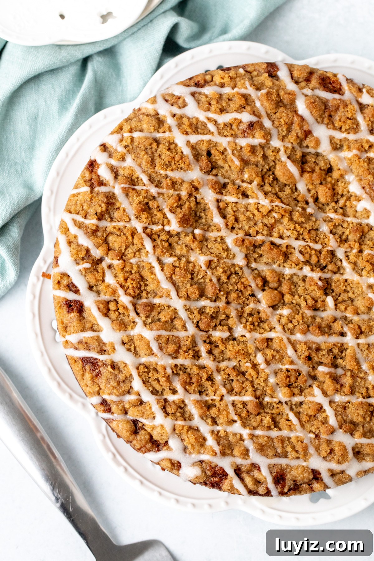 Moist Carrot Coffee Cake with Cream Cheese Glaze 3 9-inch round carrot cake with streusel topping and a drizzle of glaze on a white plate