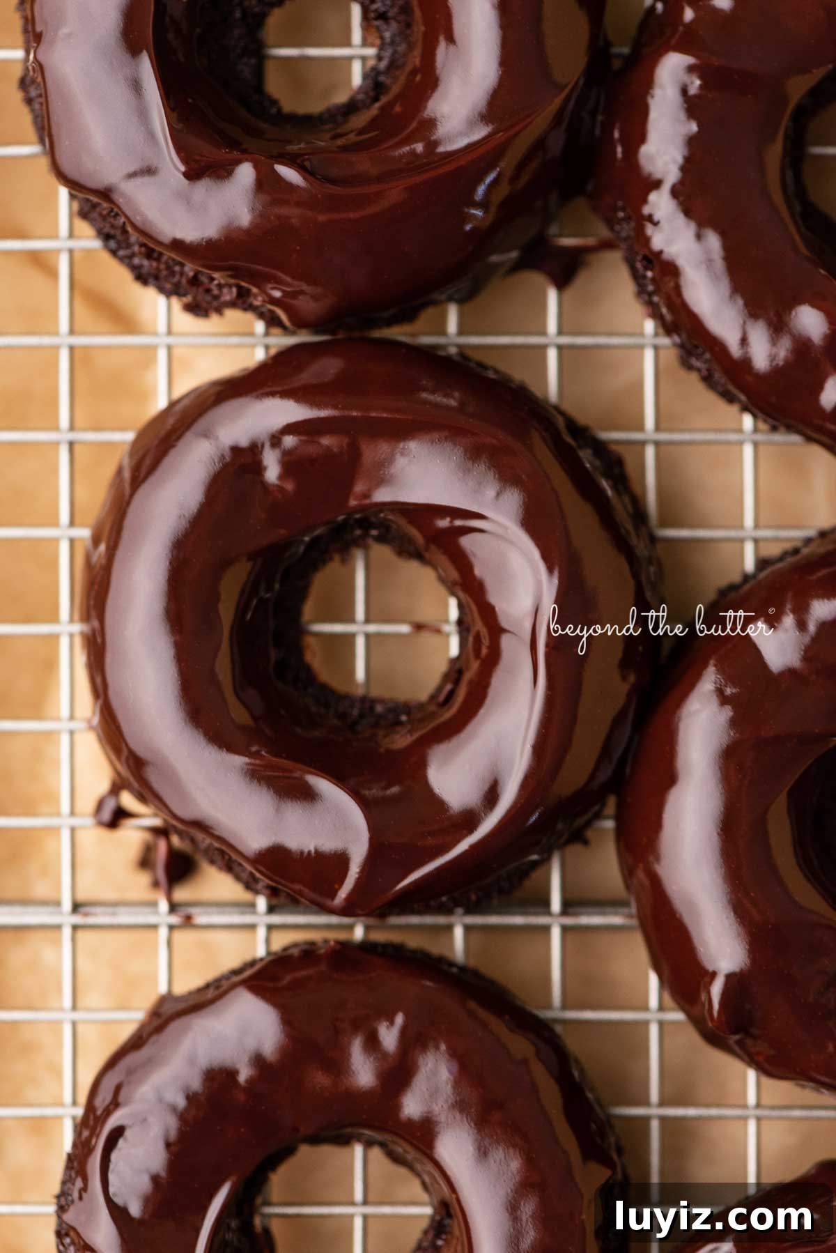 Homemade Baked Chocolate Donuts Recipe for Perfect Texture 2 Homemade baked chocolate donuts topped with chocolate ganache glaze on a wire cooling rack | © Beyond the Butter®