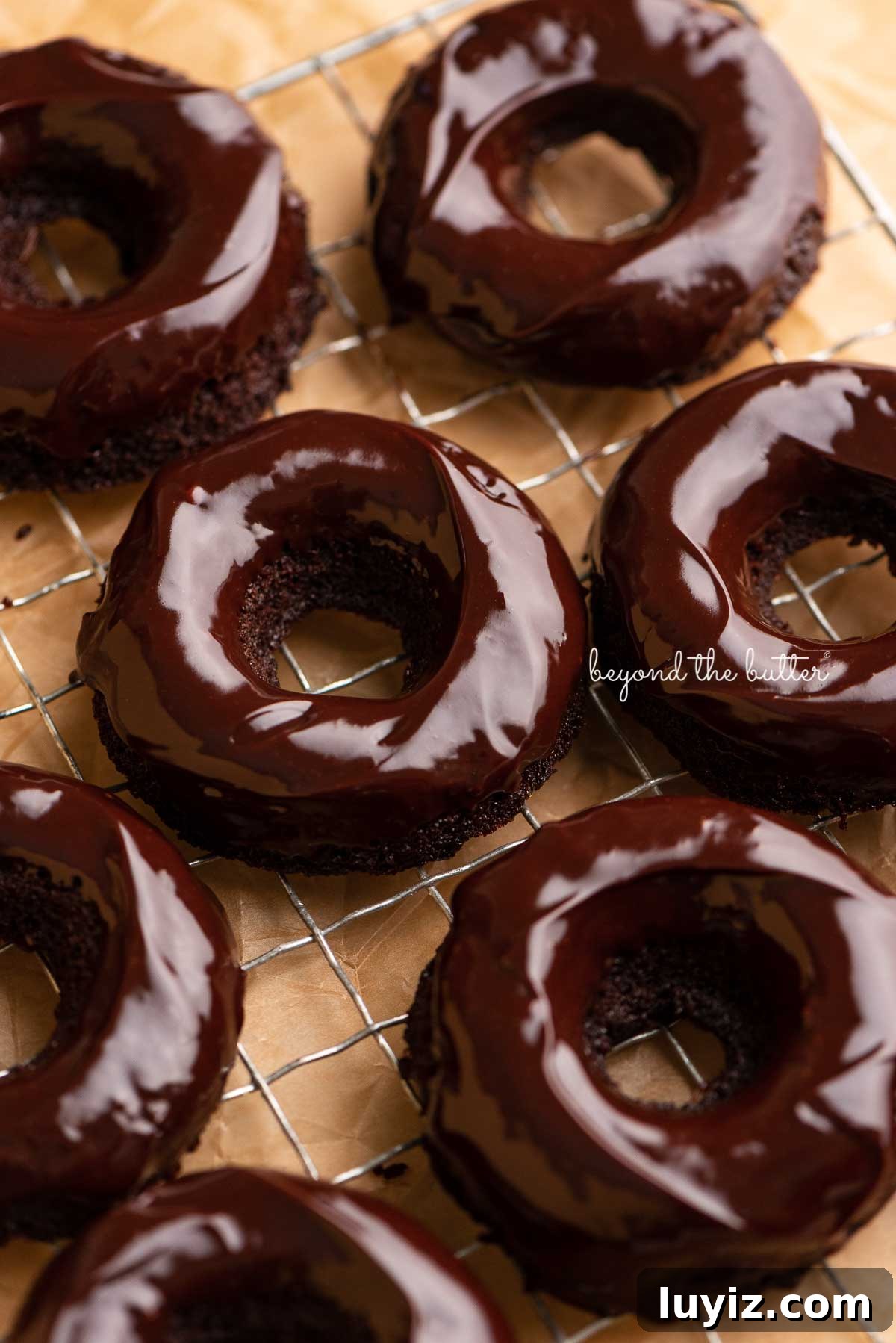 Homemade Baked Chocolate Donuts Recipe for Perfect Texture 4 Homemade baked chocolate donuts topped with chocolate ganache on a wire cooling rack | © Beyond the Butter®