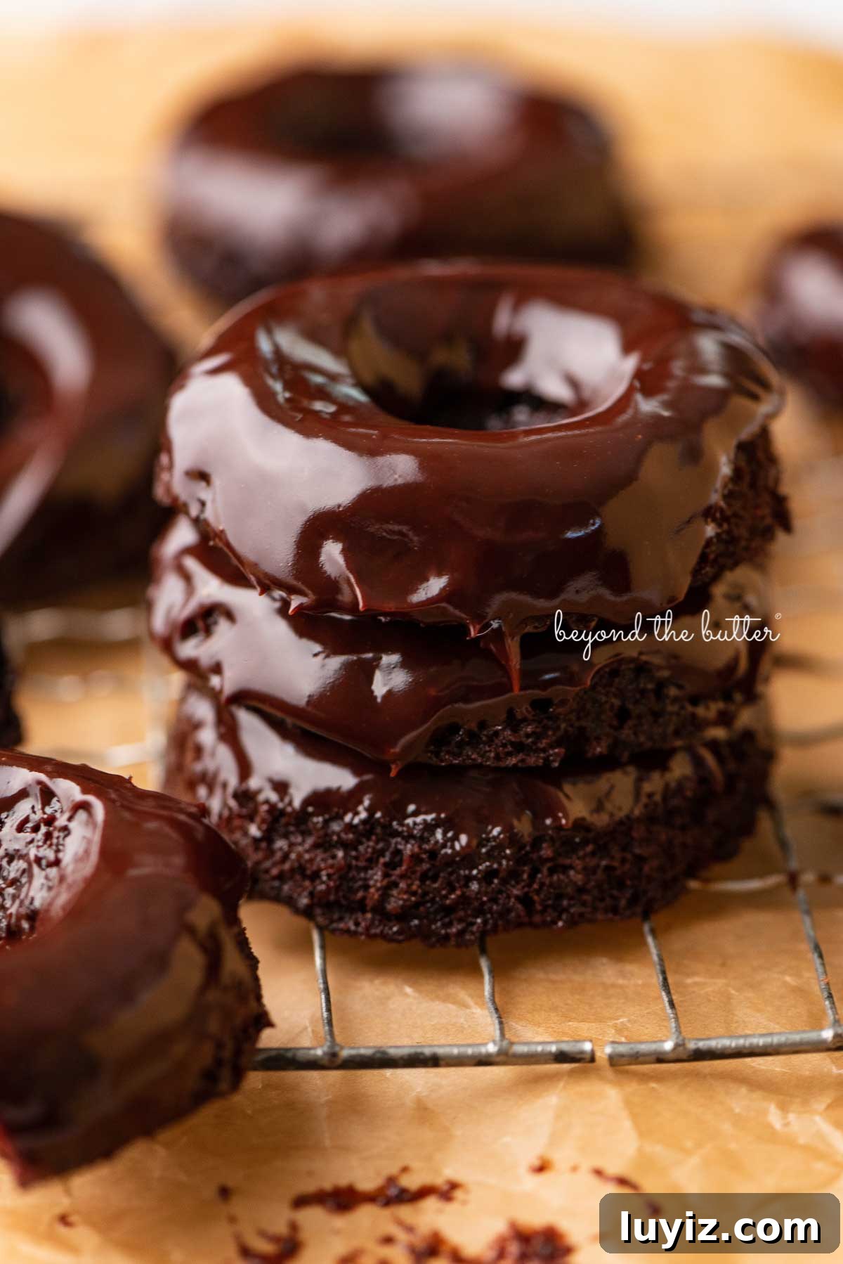 Homemade Baked Chocolate Donuts Recipe for Perfect Texture 5 Stacked homemade baked chocolate donuts topped with chocolate ganache on a wire cooling rack | © Beyond the Butter®