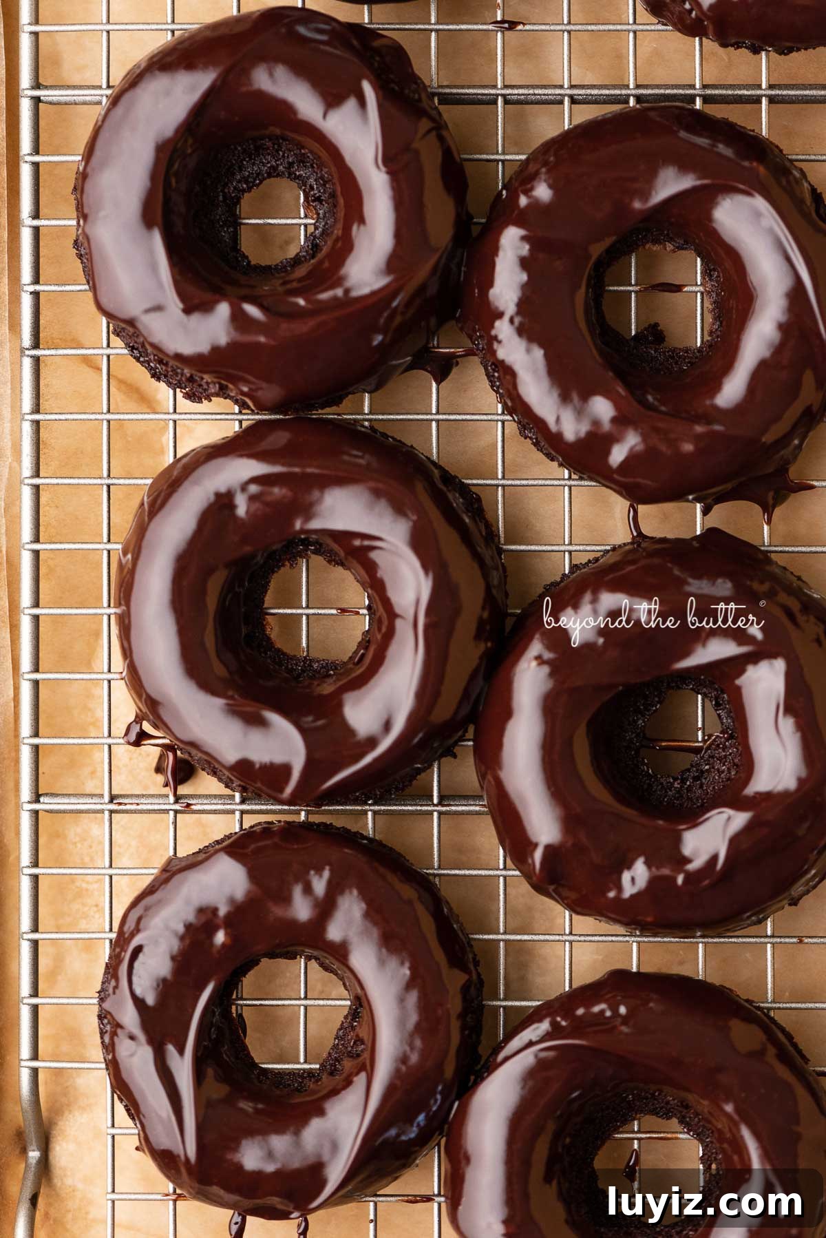 Homemade Baked Chocolate Donuts Recipe for Perfect Texture 6 Homemade baked chocolate donuts topped with chocolate ganache on a wire cooling rack | © Beyond the Butter®