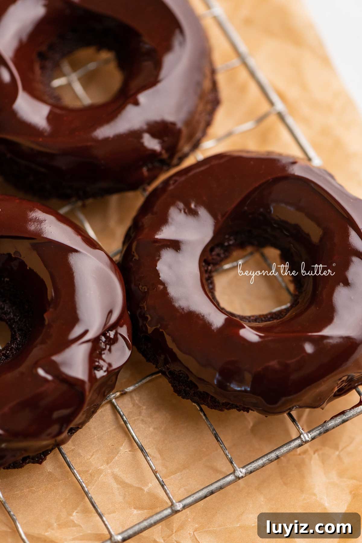Homemade Baked Chocolate Donuts Recipe for Perfect Texture 7 Homemade baked chocolate donuts topped with chocolate ganache on a wire cooling rack | © Beyond the Butter®