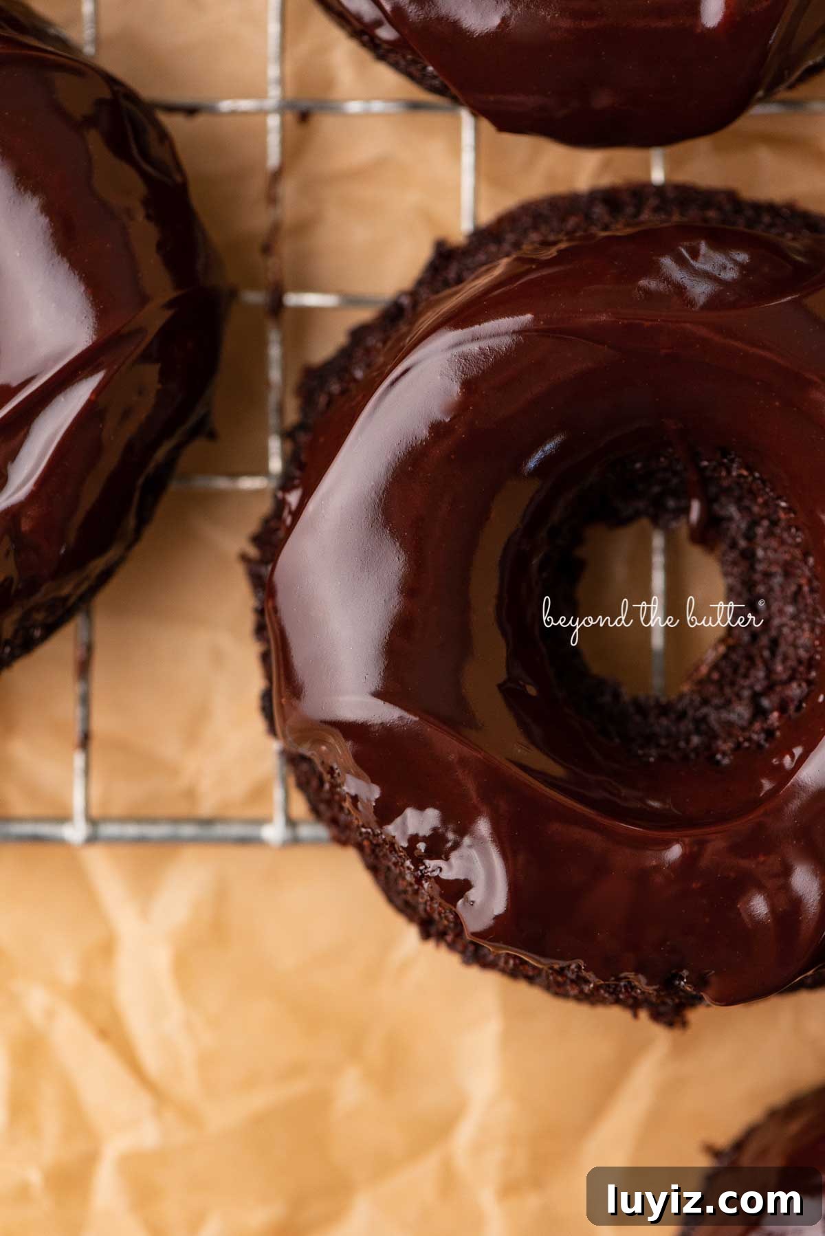 Homemade Baked Chocolate Donuts Recipe for Perfect Texture 8 Close up of homemade baked chocolate donuts topped with chocolate ganache on a wire cooling rack | © Beyond the Butter®