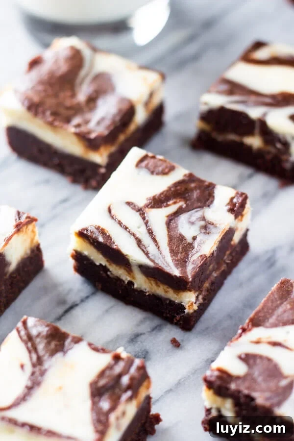 Fudgy Cream Cheese Swirl Brownies: Rich Chocolate Cheesecake Bars 5 Cream cheese brownies with swirled cheesecake layer on top cut into squares on a marble background.