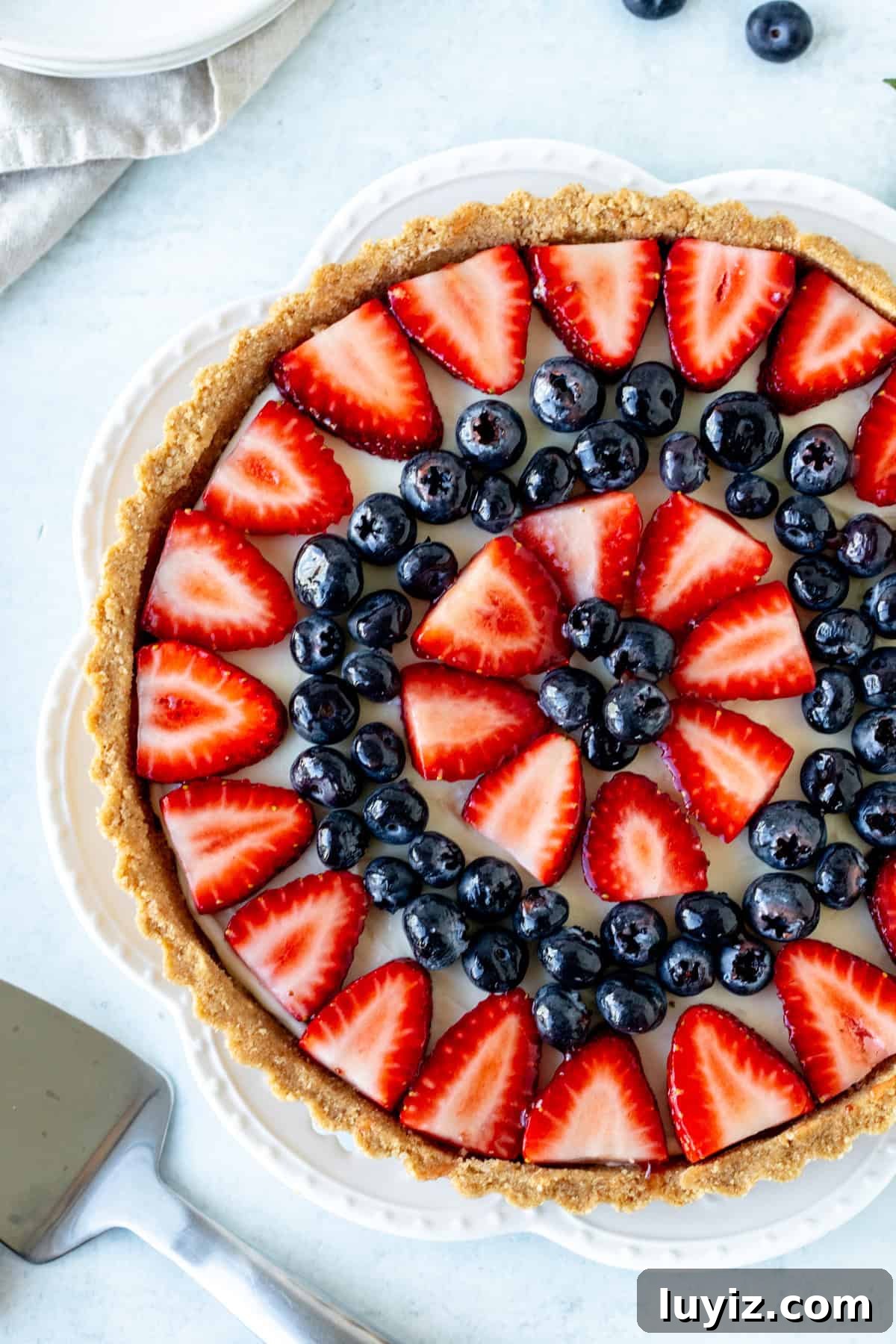 No-Bake Fresh Fruit Tart Recipe for Summer Parties 8 Fruit tart on a white plate topped with blueberries and sliced strawberries.