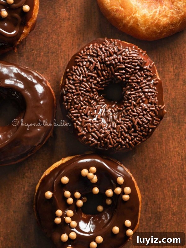 Pennsylvania Dutch Fasnacht Donuts: Traditional Recipe & History 8 Chocolate glazed decorated donuts on dark wood background.