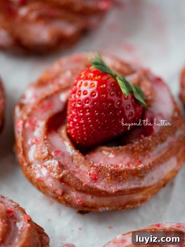 Pennsylvania Dutch Fasnacht Donuts: Traditional Recipe & History 10 Strawberry glazed french crullers on a parchment paper lined baking sheet topped with a fresh strawberry.