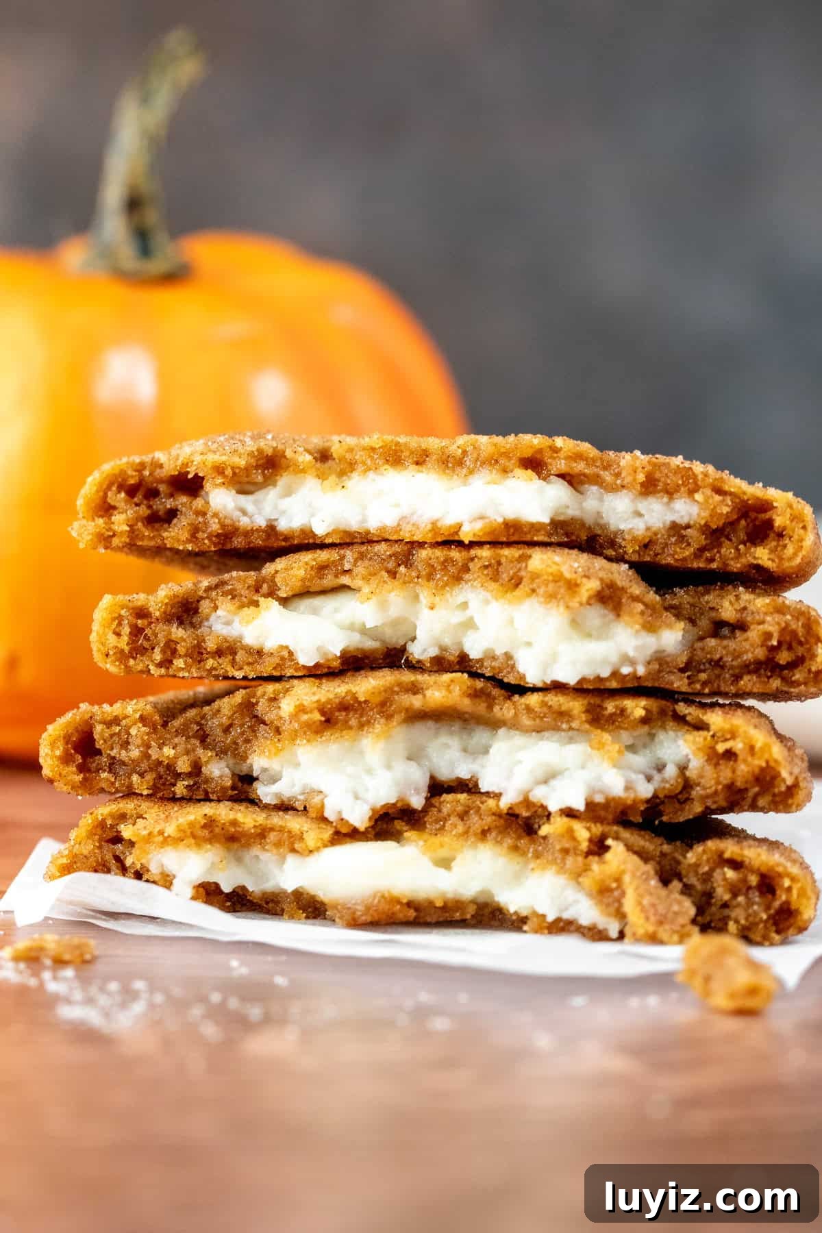 Pumpkin Cheesecake Cookie Recipe — Soft Pumpkin Cookies with Creamy Filling 8 cheesecake stuffed pumpkin cookies broken in half and stacked on top of each other