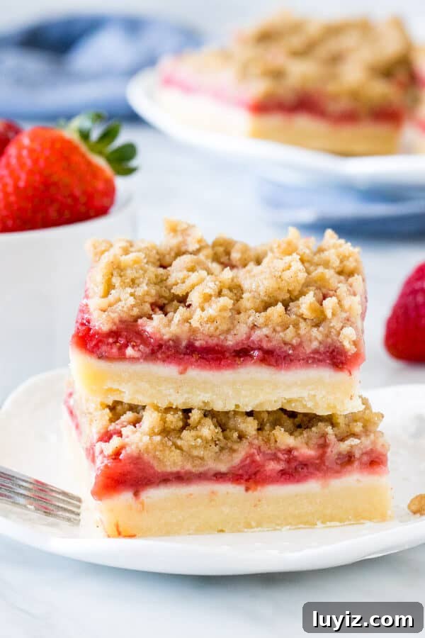 Homemade Strawberry Crumb Bars Recipe with Buttery Streusel 48 Stack of 2 strawberry crumb bars on white plate with bowl of strawberries.