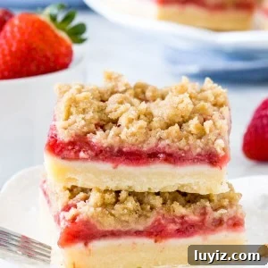 Stack of 2 strawberry crumb bars on white plate with bowl of strawberries.
