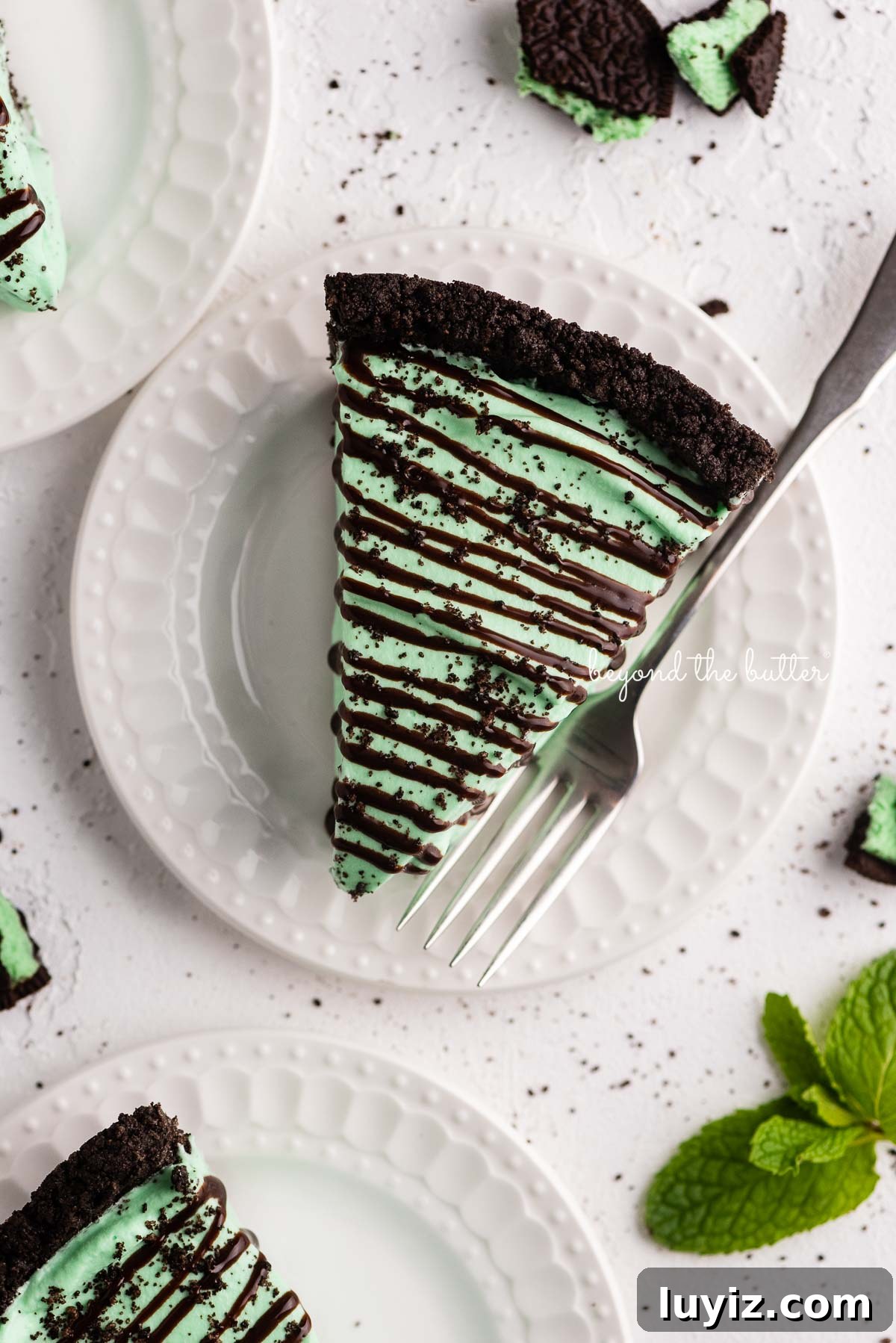 No-Bake Mint Chocolate Pie Recipe — Cool Mint Chocolate Delight 3 Dessert plates with slices of no bake mint chocolate pie with chocolate syrup drizzled over the top | © Beyond the Butter®