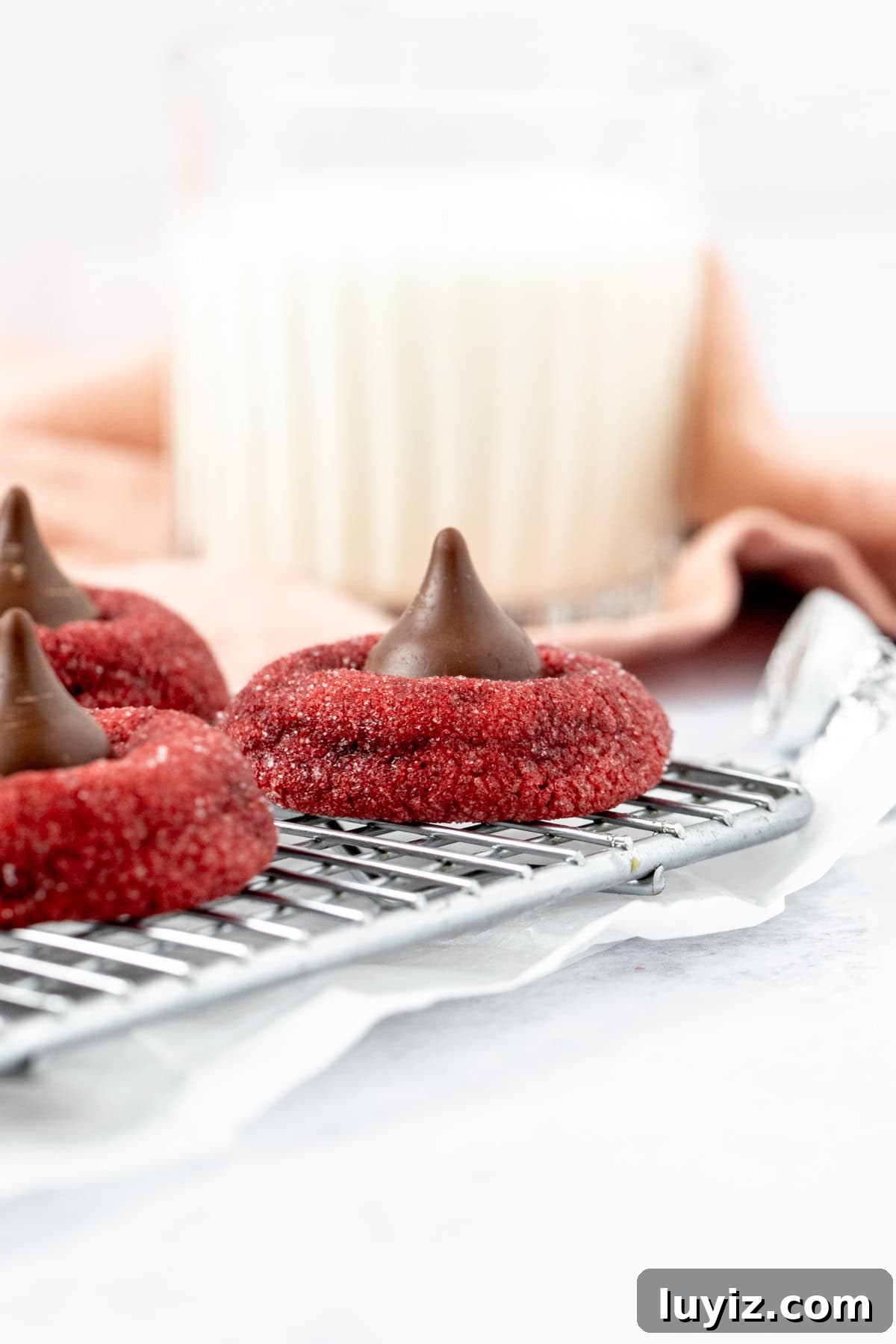 Red Velvet Blossoms: Elegant Floral Cakes and Desserts 3 Red velvet Hershey's Kiss cookies on a cooling rack with a glass of milk