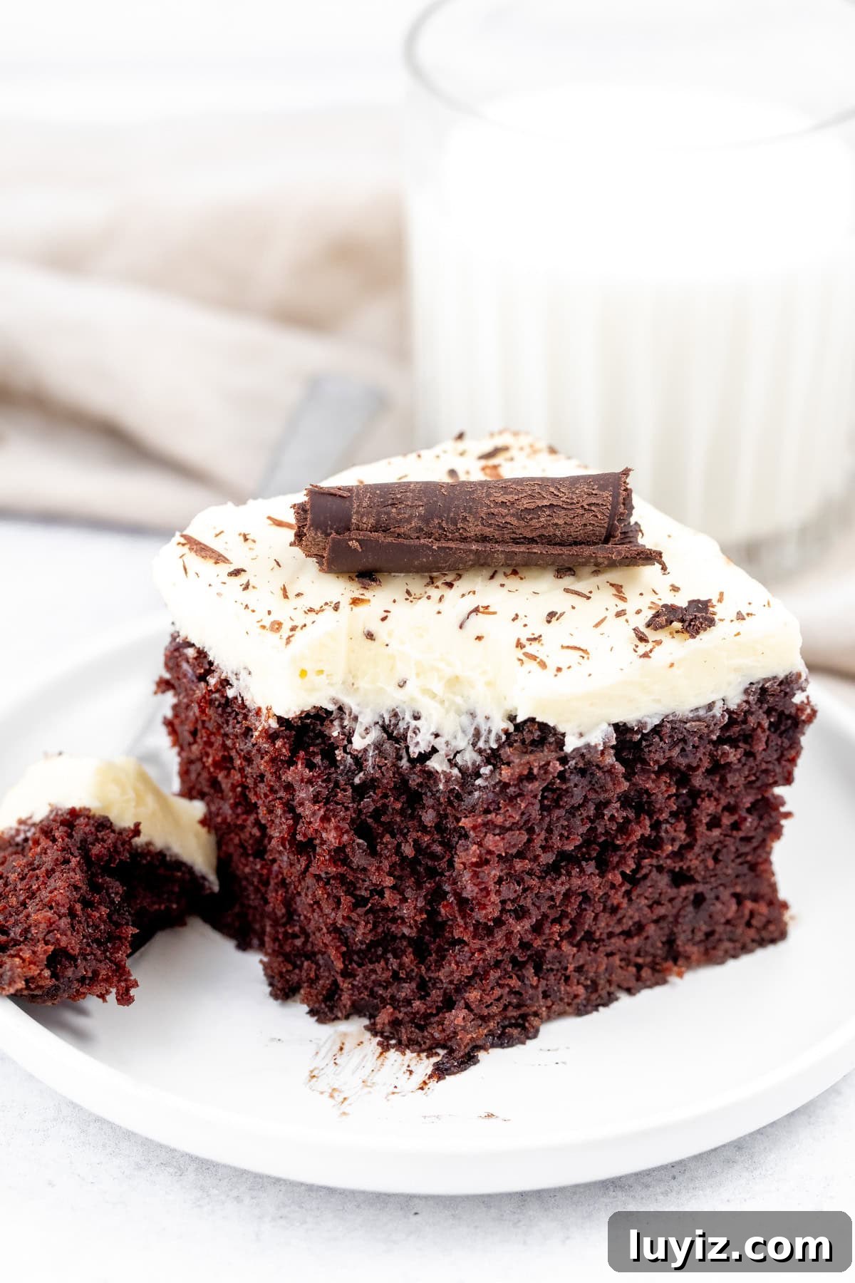 Decadent Chocolate Cake with Silky White Chocolate Frosting 3 Square piece of chocolate cake sheet cake with white chocolate frosting with a bite taken out