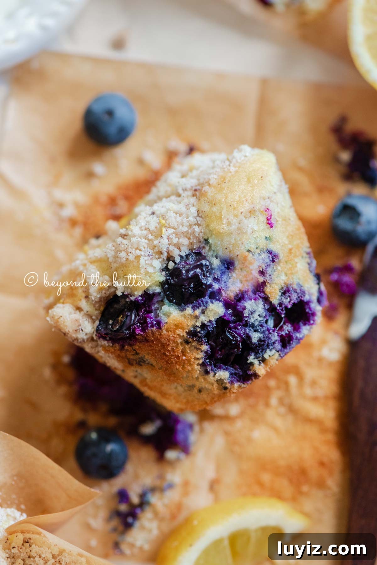 Bakery-Style Lemon Blueberry Streusel Muffins Recipe 3 Unwrapped lemon blueberry streusel muffin with lemon wedges and blueberries around it | All images © Beyond the Butter®