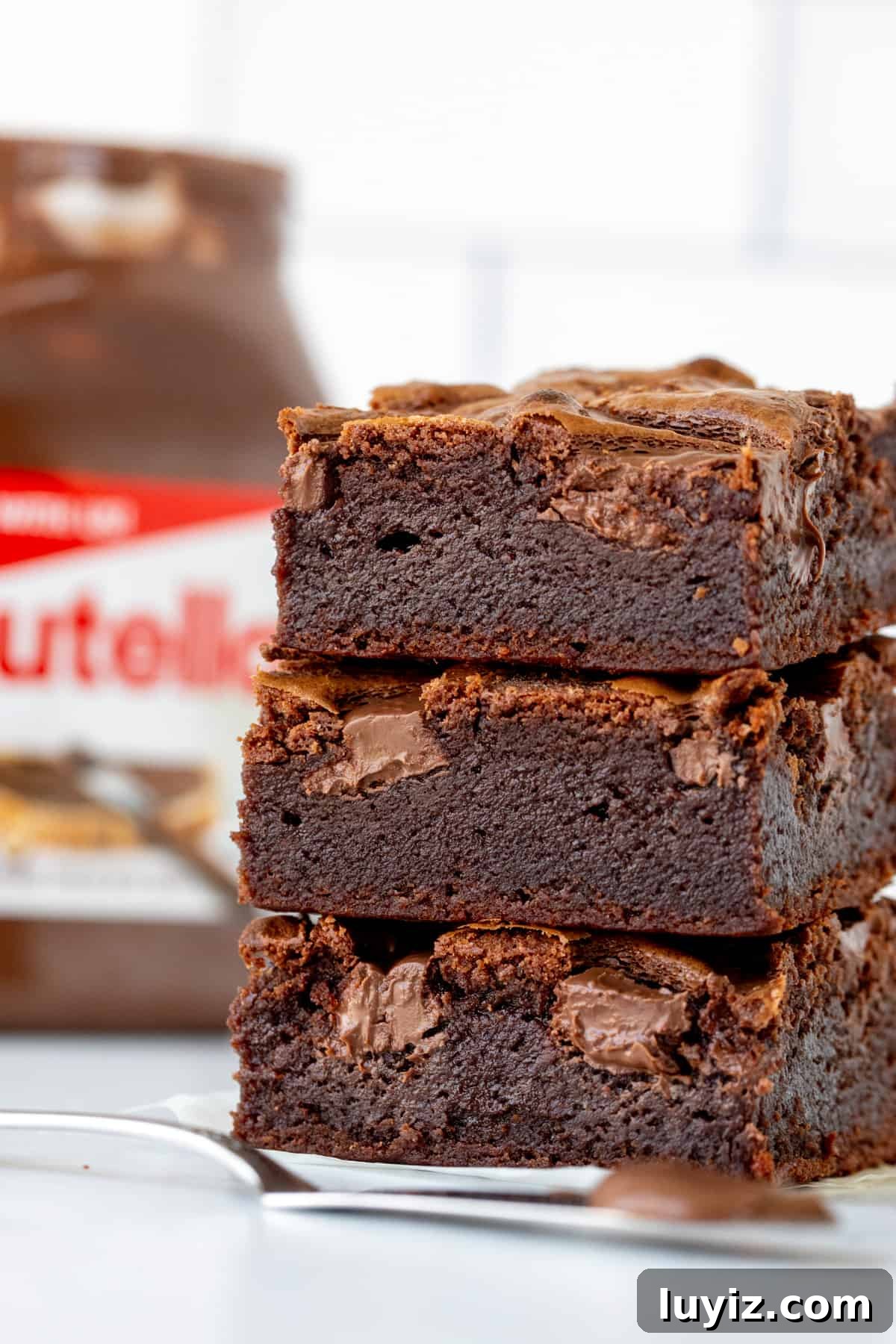Decadent Nutella Brownies Recipe with Gooey Chocolate Swirls 2 Stack of three Nutella brownies with jar of Nutella