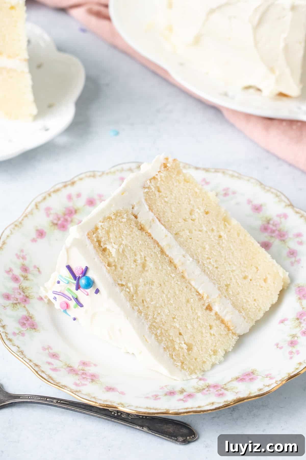 Classic White Cake Recipe: Moist, Fluffy Celebration Cake 3 Slice of 2 layer white cake with vanilla frosting on a plate, on its side