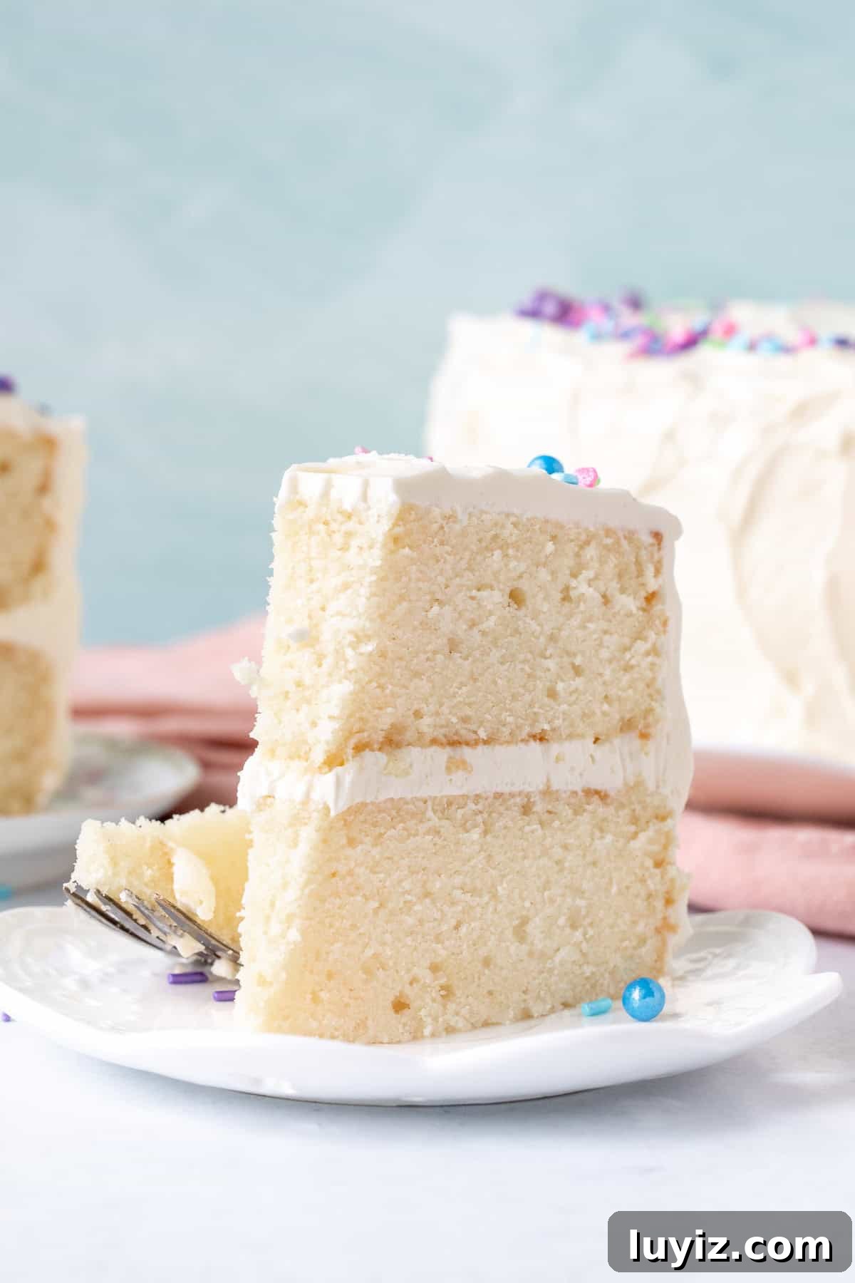 Classic White Cake Recipe: Moist, Fluffy Celebration Cake 5 Slice of white vanilla cake with vanilla frosting with a bite taken out