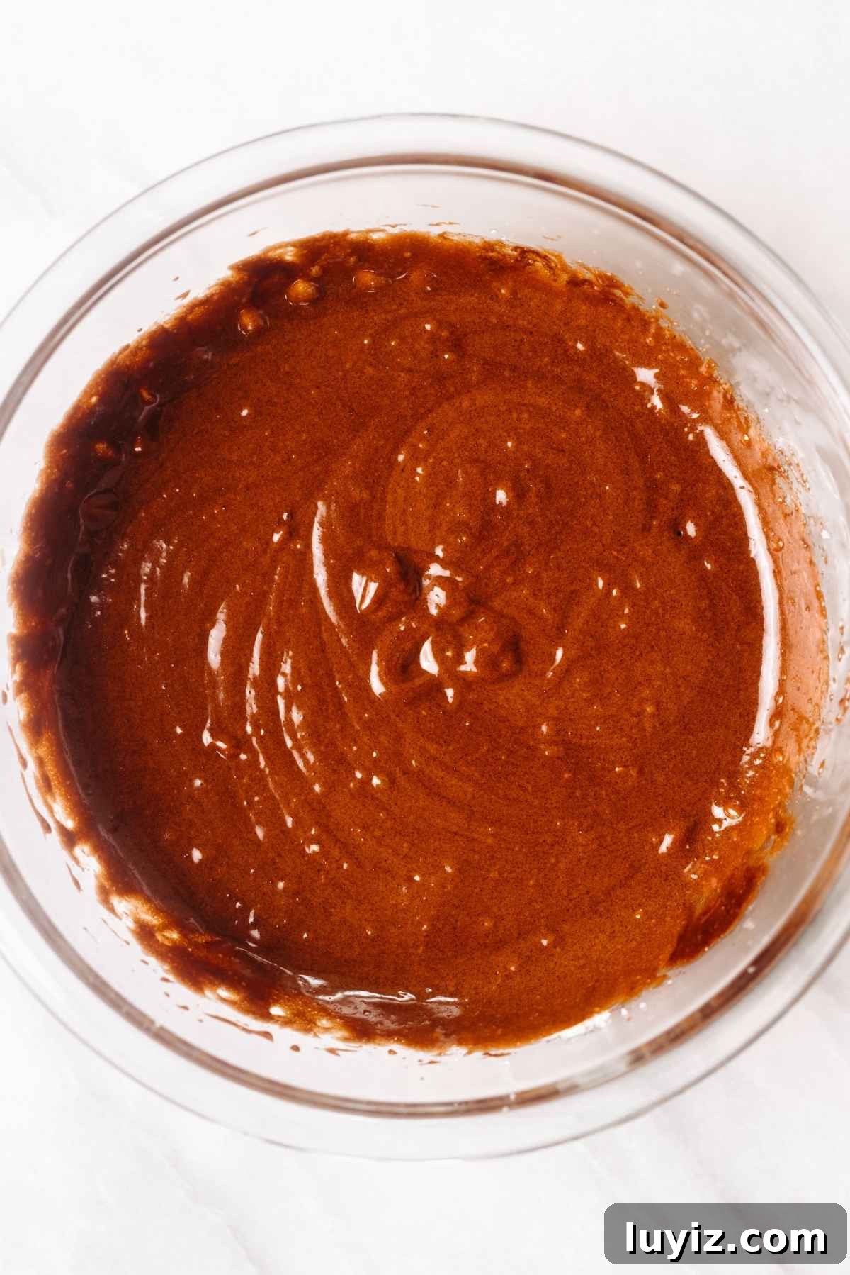 Fudgy Brownie Bites Recipe — Moist Mini Chocolate Brownies 11 Brownie bites wet ingredients blended together in a large glass mixing bowl on a white textured background.