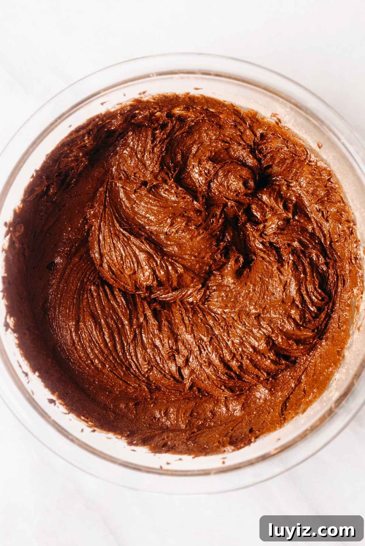 Fudgy Brownie Bites Recipe — Moist Mini Chocolate Brownies 12 Brownie batter in a large glass mixing bowl on a white textured background.